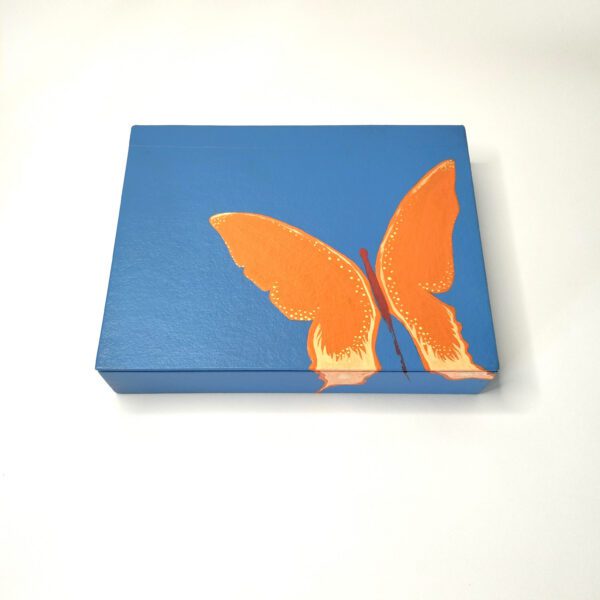 Organize seu espaço com esta caixa artesanal azul com borboleta laranja, tamanho grande, com 8 divisórias. Está exposta fechada sobre um fundo branco.