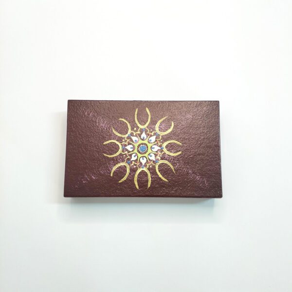 Caixa artesanal castanha com mandala, tamanho médio, com 3 divisórias, está exposta fechada sobre um fundo branco.
