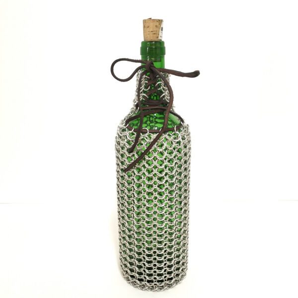 Transforme as suas garrafas em peças únicas com esta capa artesanal em cota de malha. Feita com argolas metálicas. Está exposta sobre um fundo branco.