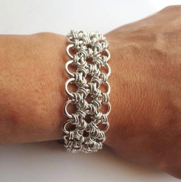Esta pulseira artesanal em cota de malha inspira-se no design japonês. Está colocada no pulso, é um close-up da pulseira a ser usada, o fundo da imagem é branco.