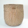 Cesta artesanal multiusos natural e laranja média em folha de palma. Padrão em zigue-zague. Está exposta sobre um fundo branco.