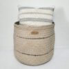 Cesta artesanal média natural em folha de palma com duas filas de furos. Está com uma almofada dentro, sobre um fundo branco.