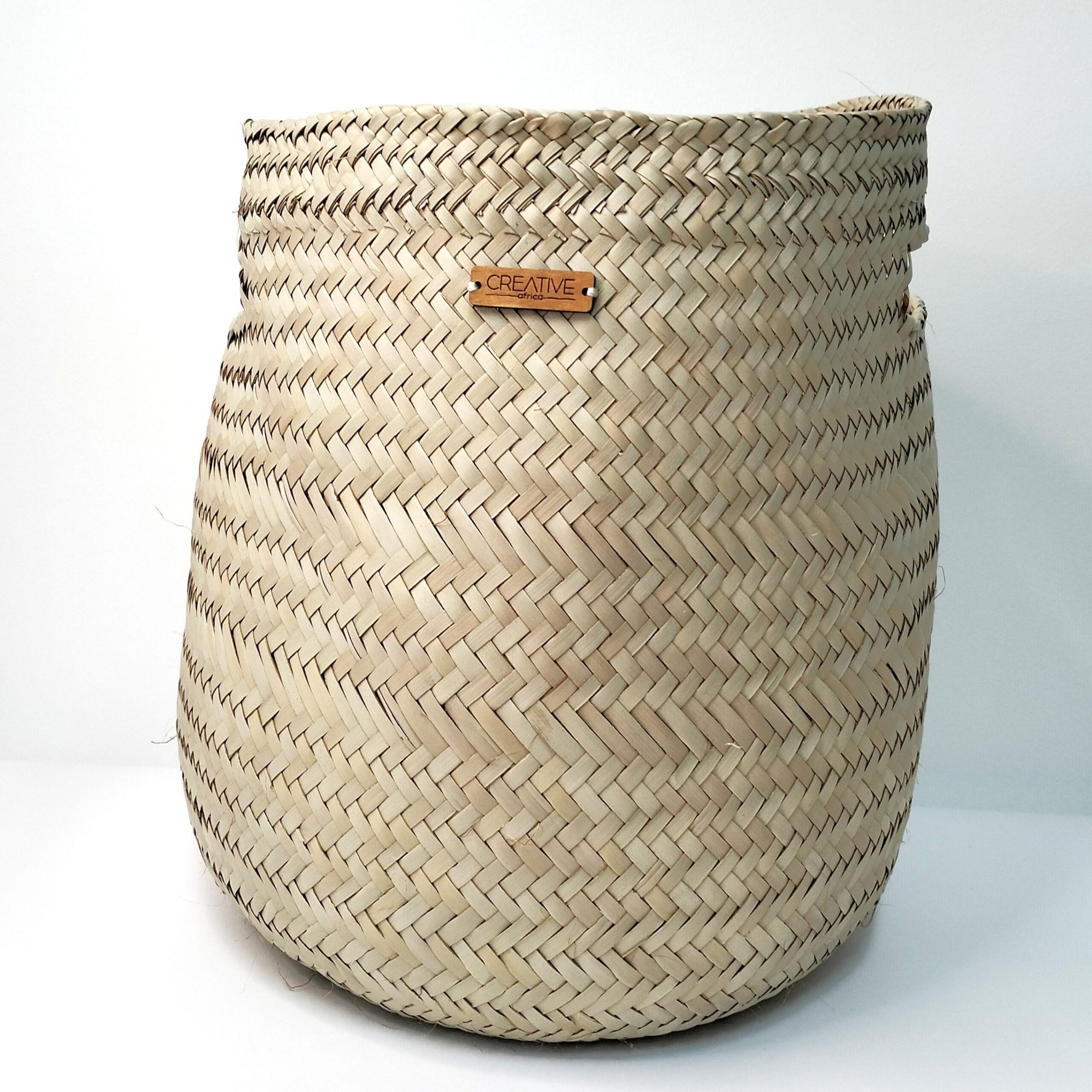 Cesta artesanal multifunções em folha de palma com pegas. Está exposta sobre um fundo branco.
