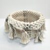 Cesto multiusos em macramé, está sobre um fundo branco.