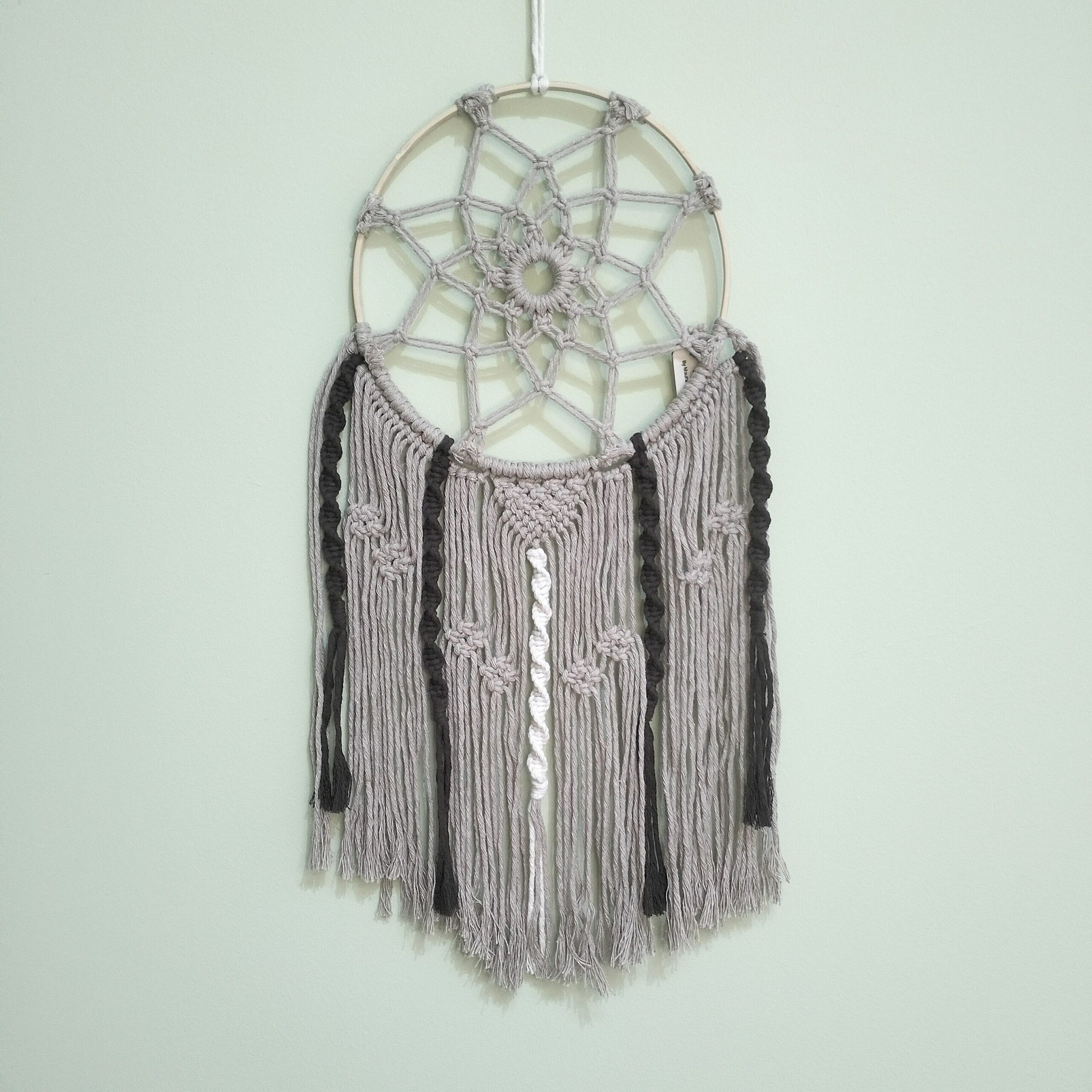 Caçador de sonhos artesanal em macramé castanho e bege. Está exposto numa parede verde claro.
