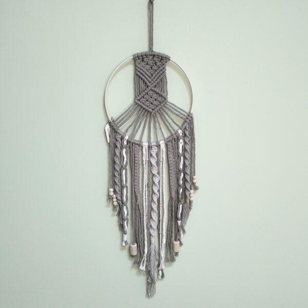 Caçador de sonhos artesanal em macramé nas cores natural e bege. Está exposto numa parede verde claro.