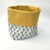 Cesto de tecido 100% algodão com padrão azul e amarelo e forro liso amarelo que se vê na dobra ajustável em altura. Está sobre um fundo branco.