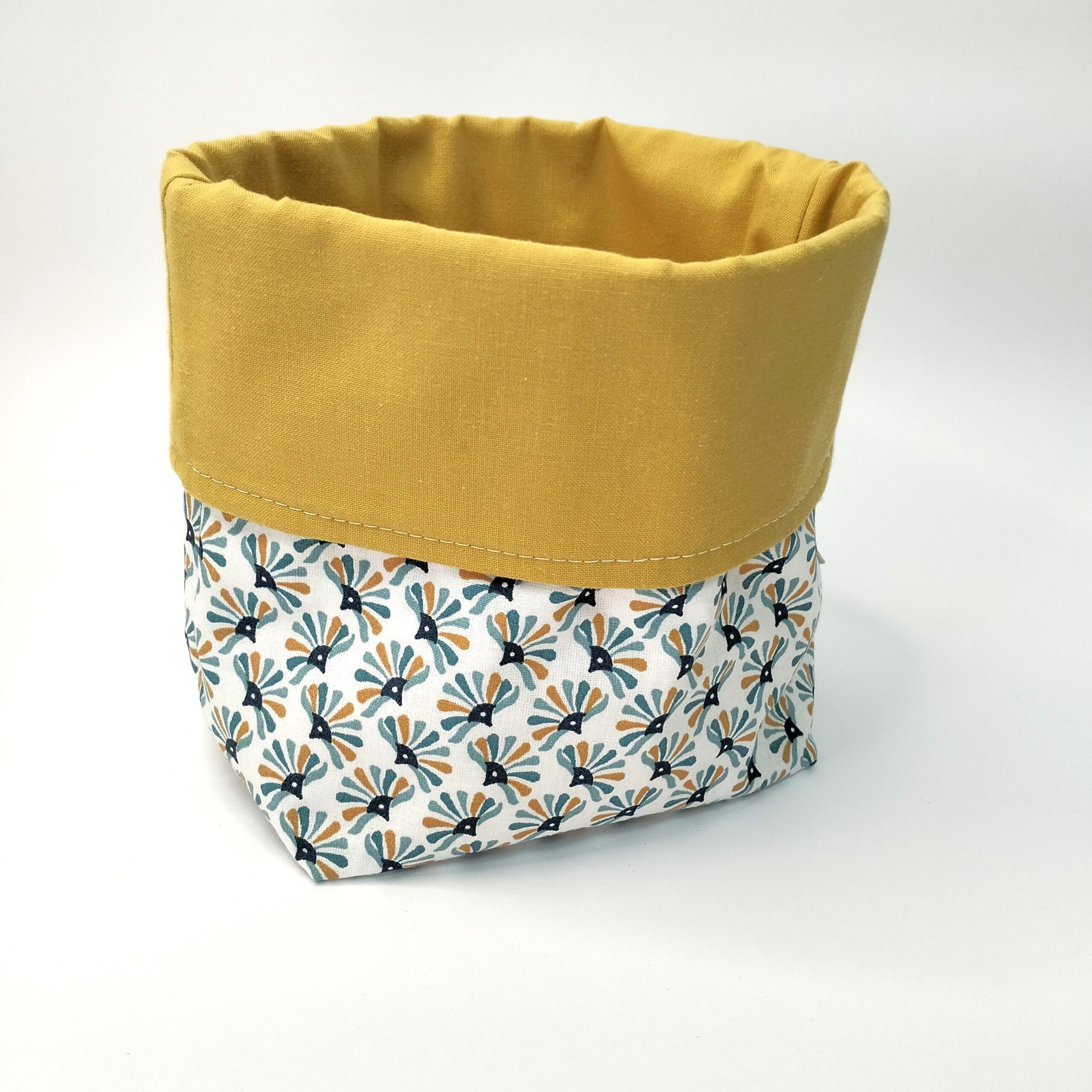 Cesto de tecido 100% algodão com padrão azul e amarelo e forro liso amarelo que se vê na dobra ajustável em altura. Está sobre um fundo branco.