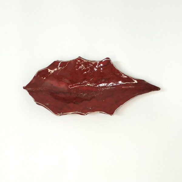 Folha de azevinho artesanal em cerâmica vidrada de vermelho. Está sobre um fundo branco.