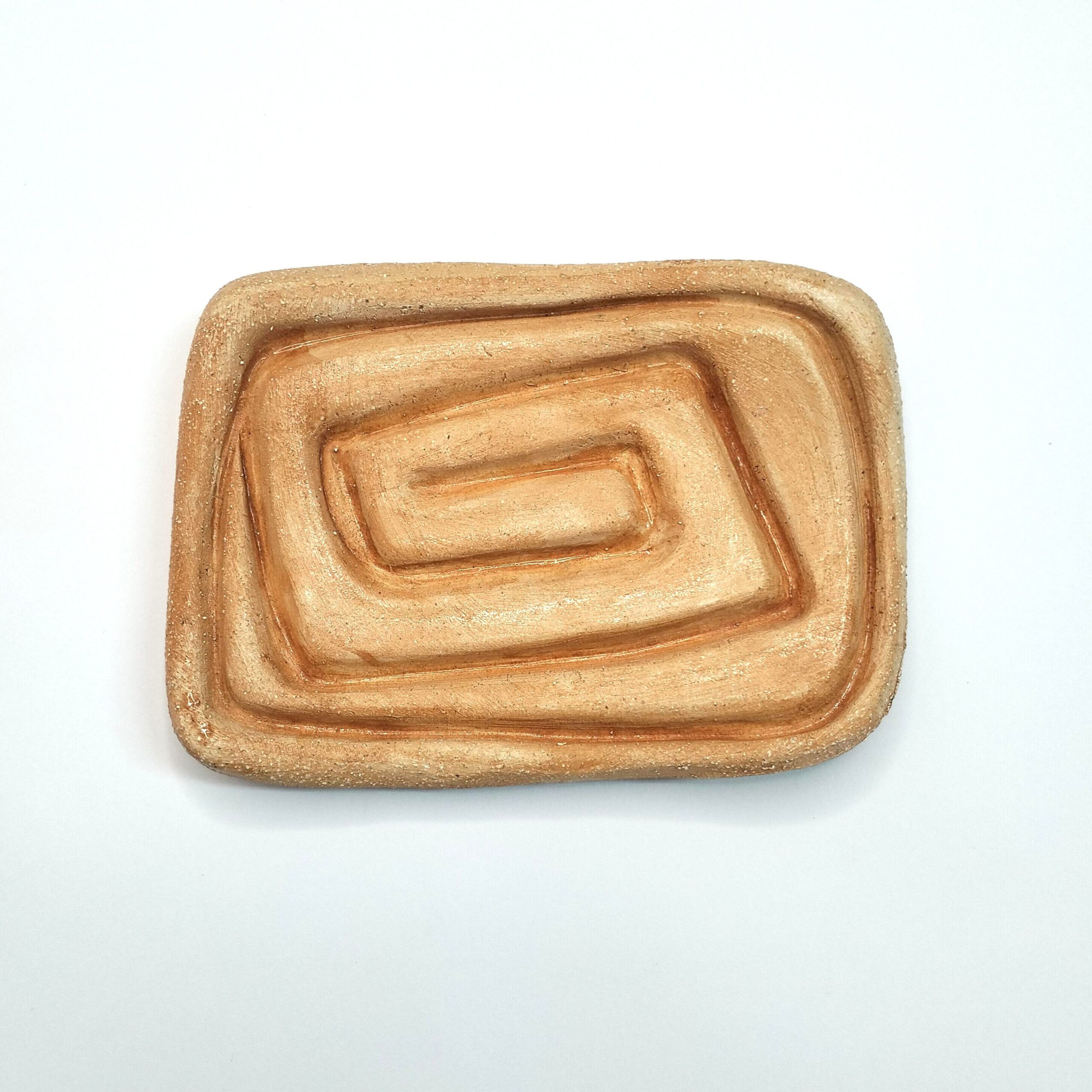 Saboneteira artesanal em cerâmica na cor salmão com efeito espiral. Está sobre um fundo branco.