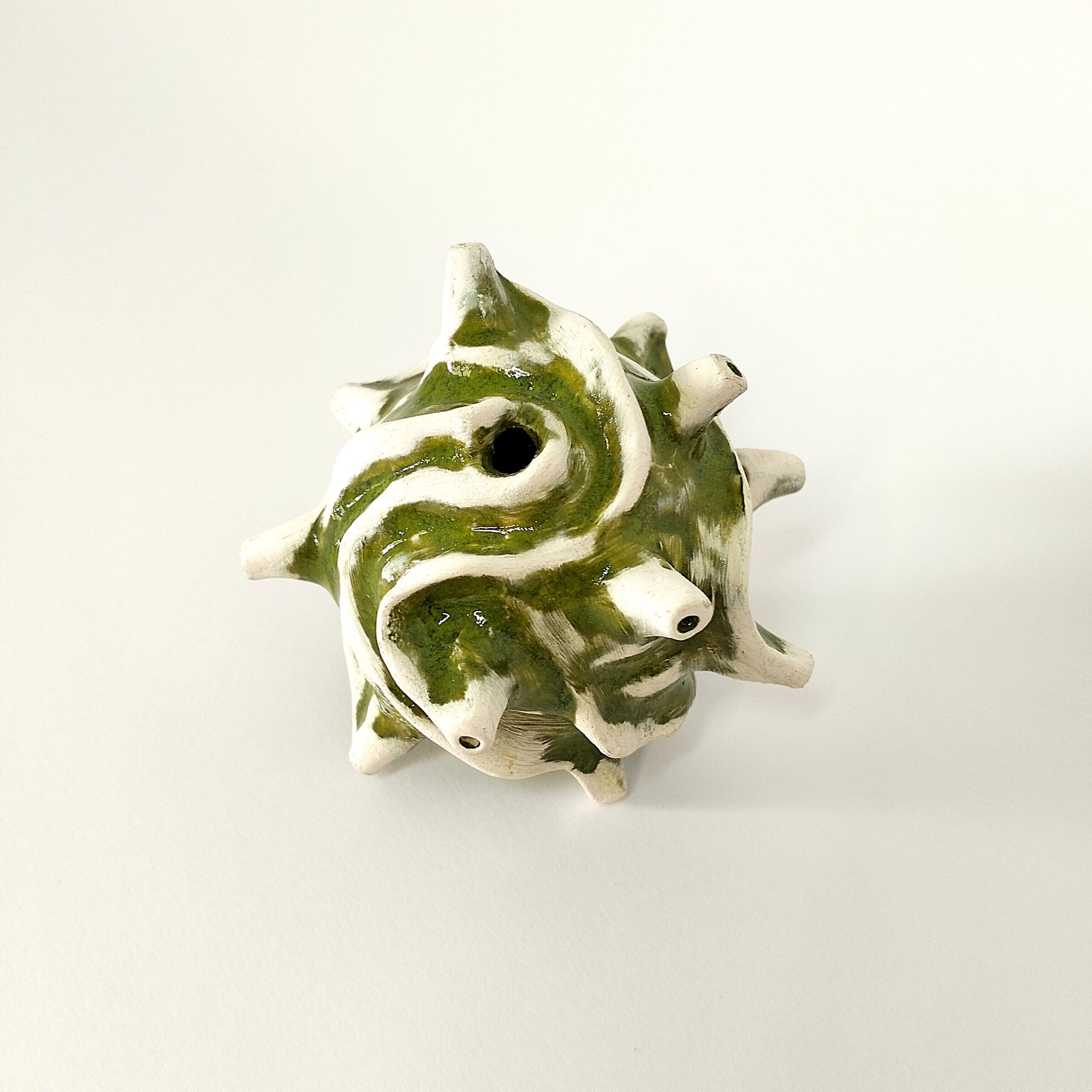 Escultura artesanal "Semente"  em cerâmica vidrada verde. Está exposta sobre um fundo branco.