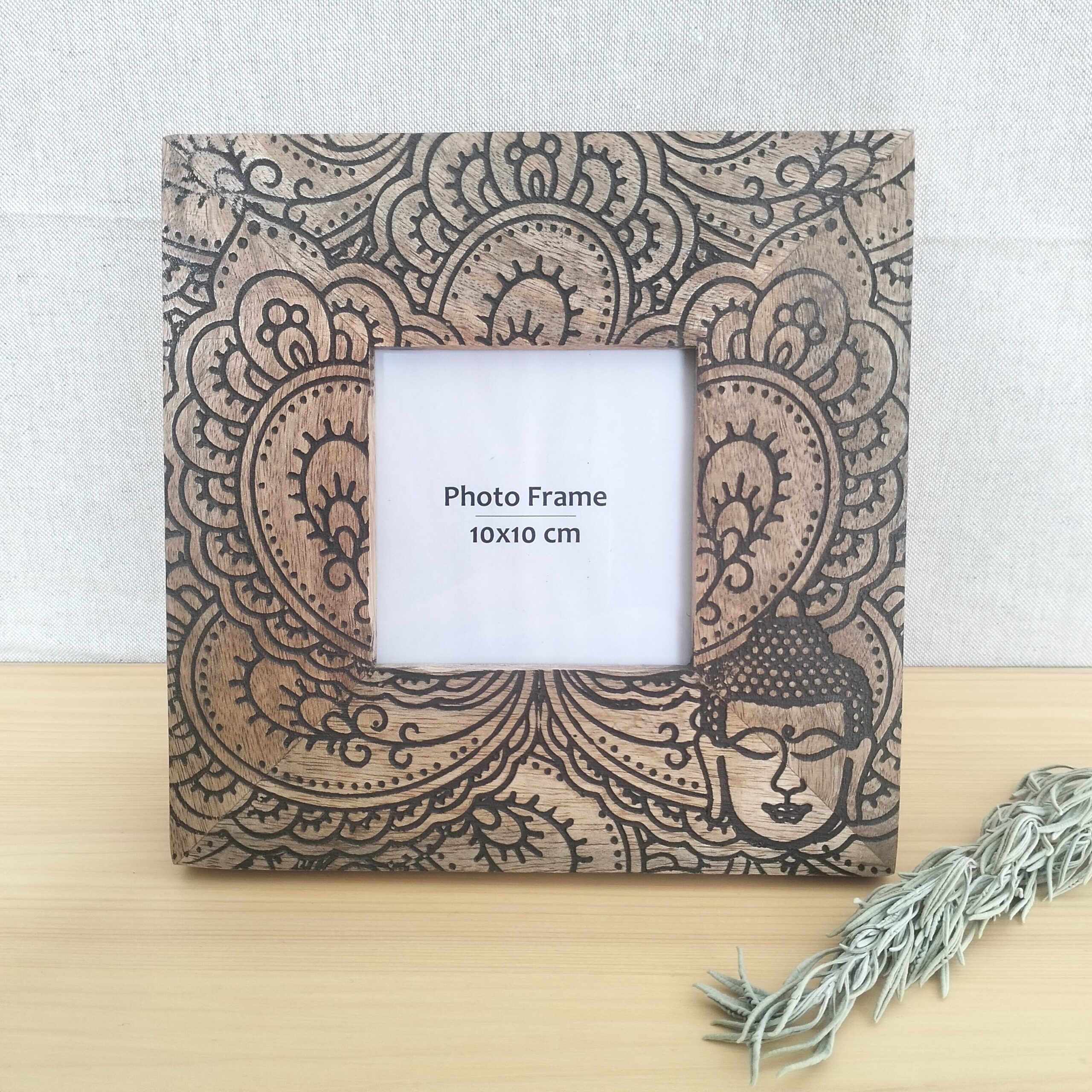 Moldura artesanal em madeira de manga pirogravada para fotografia de 10x10cm. Está sobre uma prateleira com um raminho de alfazema ao lado.
