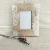 Moldura artesanal em madeira de manga pirogravada para fotografia de 10x10cm. Está sobre um fundo de tecido bege com um raminho seco ao lado.