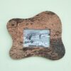 Moldura artesanal em cortiça para fotografia 10x15 cm com formato ondulado orgânico. Leve, natural e ideal para decoração de parede. Está colocada numa parede verde claro.