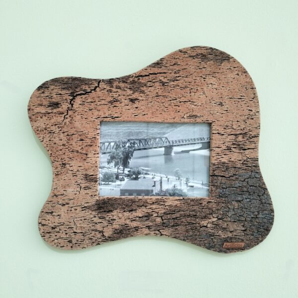 Moldura artesanal em cortiça para fotografia 10x15 cm com formato ondulado orgânico. Leve, natural e ideal para decoração de parede. Está colocada numa parede verde claro.