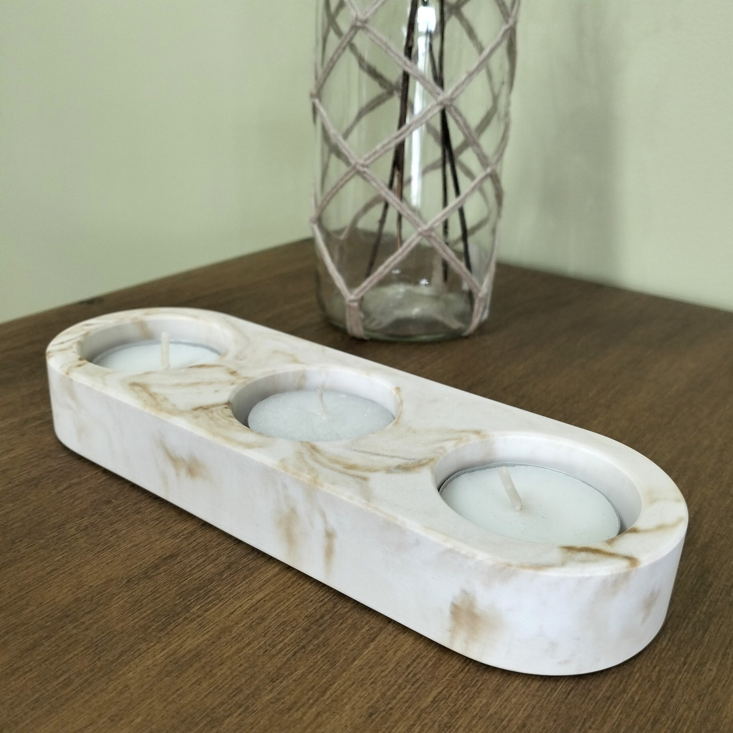 Castiçal em resina ecológica em tons de areia para 3 velas tealight. Está sobre madeira com um jarra por trás.
