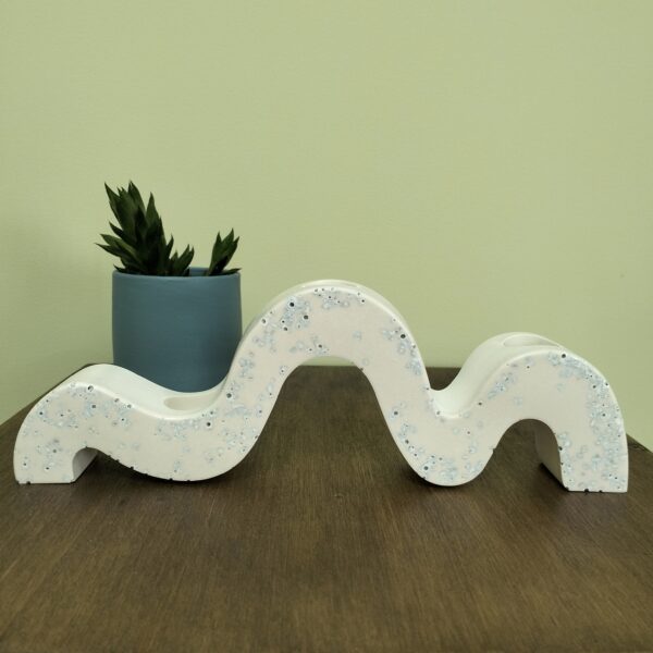 Castiçal "Ondas" em resina ecológica para 3 velas finas. Tem pormenores em azul suave. Está sobre uma madeira com um vaso azul com suculenta atrás.