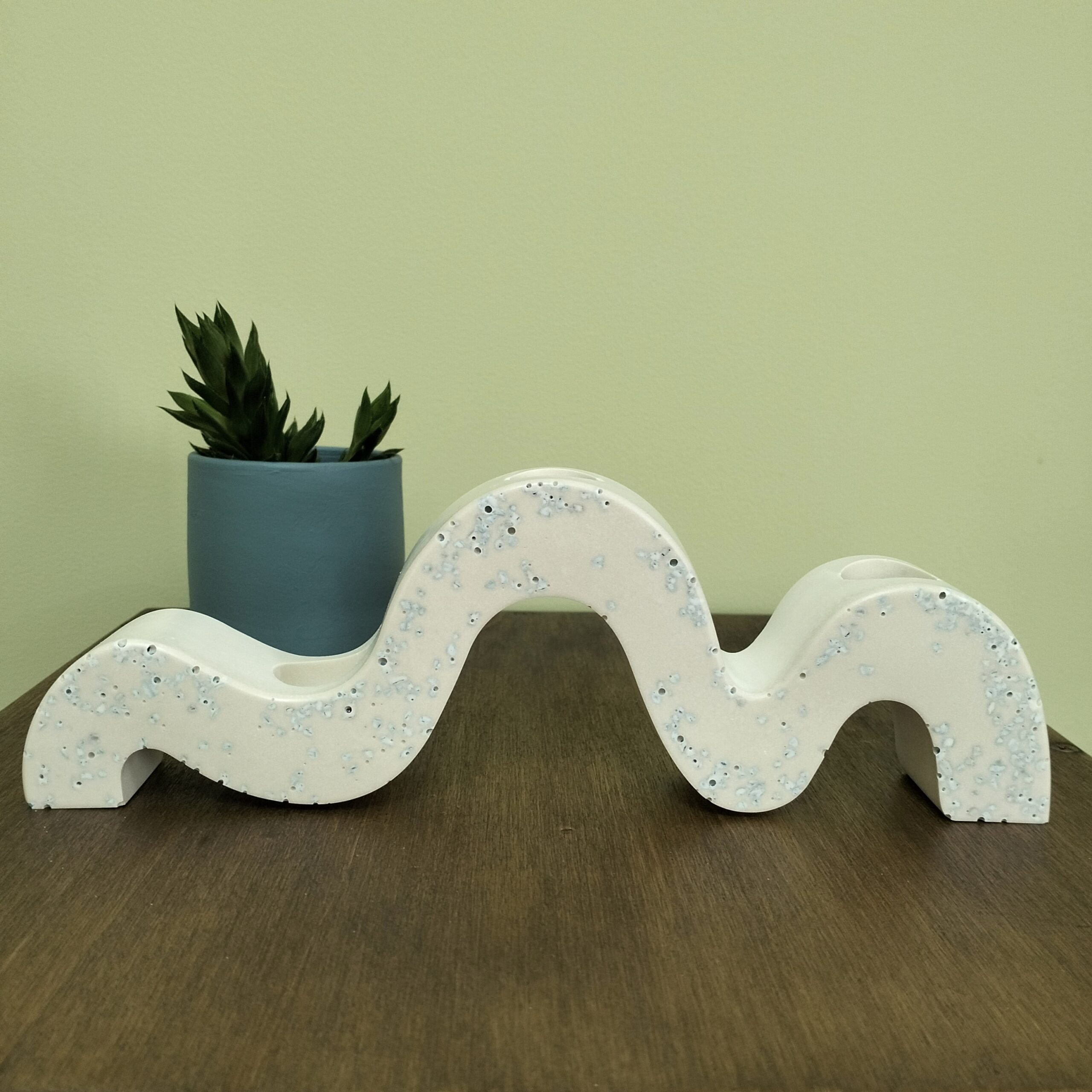 Castiçal "Ondas" em resina ecológica para 3 velas finas. Tem pormenores em azul suave. Está sobre uma madeira com um vaso azul com suculenta atrás.