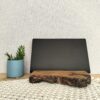 Tablet colocado num suporte artesanal em madeira de sobreiro adequado para o efeito. Está sobre uma peça de macramé e um pequena planta ao lado.